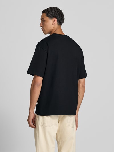 Männermodel trägt T-Shirt mit Statement-Print und Rundhalsausschnitt von Redefined Rebel aus Baumwoll-Mix, Relaxed-Fit, Modell 'Bruno', schwarze Farbe, Rückenansicht, Ganzkörperansicht Rückansicht.