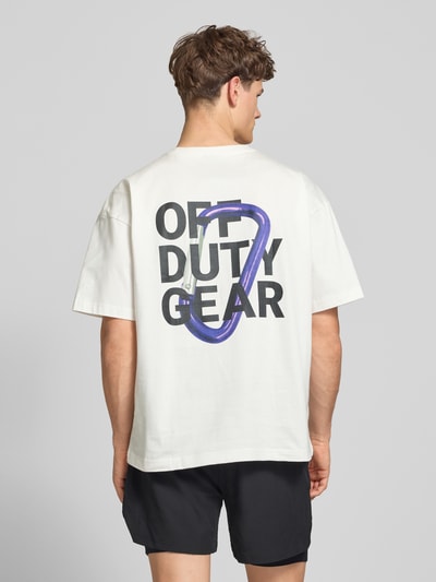 Männermodel trägt Boxy Fit T-Shirt mit Label-Print von ELITE in Weiß, schwarze Schrift, reine Baumwolle, Ganzkörperansicht Rückansicht.