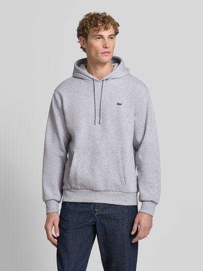 Męski model nosi Relaxed Fit Hoodie aus Baumwoll-Mix od Lacoste, jasnoszara bluza z kapturem, gładka faktura, Ganzkörperansicht von vorne. Bluza męska Lacoste