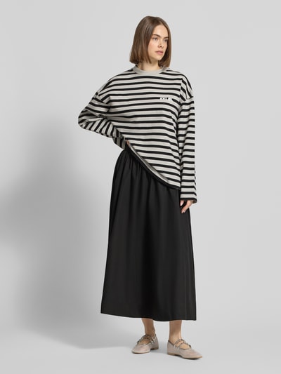 Frauenmodel trägt schwarzen Midirock mit seitlichem Reißverschluss Modell 'SALLY' von Topshop aus reiner Baumwolle, A-Linie, Ganzkörperansicht von vorne. Bundweite bei Größe 36: 35 cm.