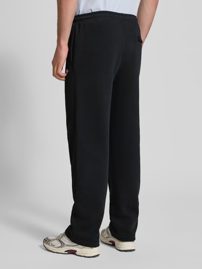 Männermodel trägt Sweatpants mit Logo-Stitching und Eingrifftaschen von Nike aus Baumwoll-Mix, Loose-Fit, Schwarz, Ganzkörperansicht Rückansicht.