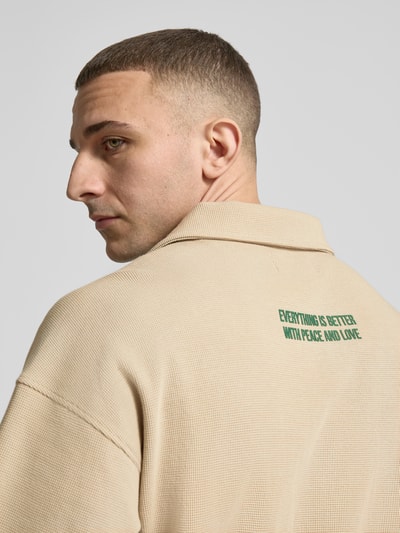Männermodel trägt Regular Fit Poloshirt mit Logo-Detail von ANOTHER COTTON LAB, beiger Baumwoll-Mix mit Strukturmuster, Ganzkörperansicht Rückansicht.