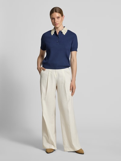 Frauenmodel trägt Regular Fit Poloshirt aus Viskose-Mix Modell 'JAMBER' von Essentiel Antwerp in Dunkelblau mit kontrastfarbenem Kragen, kombiniert mit heller, weiter Hose; Ganzkörperansicht von vorne.