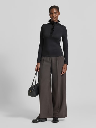 Modelka nosi czarną bluzkę z długim rękawem 'Longsleeve mit Rüschen' od Rich & Royal, mieszanka lyocellu i bawełny, taliowany krój, kołnierz z krytą listwą guzikową, falbany, długość tyłu w rozmiarze 36: 60 cm, pełny widok z przodu.