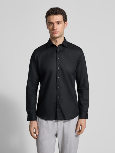 Męski model nosi Regular Fit Freizeithemd aus Leinen-Mix von Jake*s, czarna barwa, kołnierzyk typu kent, mieszanka bawełny i lnu, długość tyłu 75 cm, szerokość w rozmiarze M 50 cm, długość rękawów 66 cm, listwa guzikowa, widok całej sylwetki z przodu.