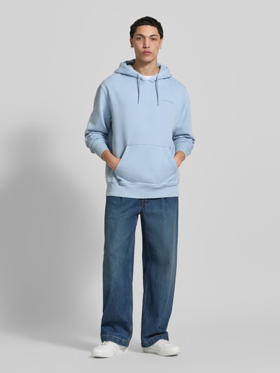 Männermodel trägt hellblauen Hoodie mit Label-Stitching und Känguru-Tasche von Dickies, Relaxed Fit, Ganzkörperansicht von vorne.