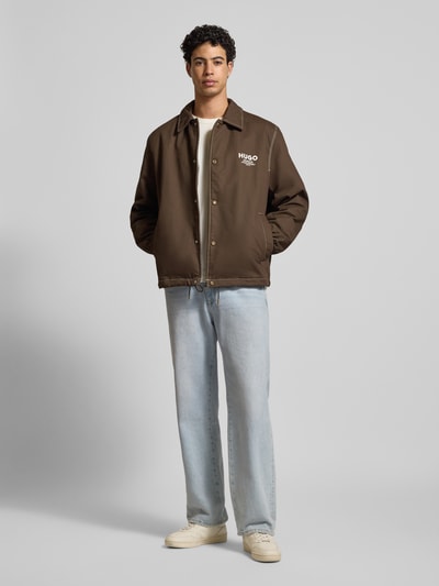 Męski model nosi Regular Fit Blouson aus reiner Baumwolle Modell 'BIYO2611' od HUGO BLUE, efekt: jednolity kolor, krój regular fit, wykładany kołnierz, zatrzaski, nadruk z logo, szwy w kontrastowym kolorze, długi rękaw, elastyczne zakończenie rękawów, tunel u dołu, wpuszczane kieszenie, kieszeń wewnętrzna, materiał: bawełna. Ganzkörperansicht von vorne.