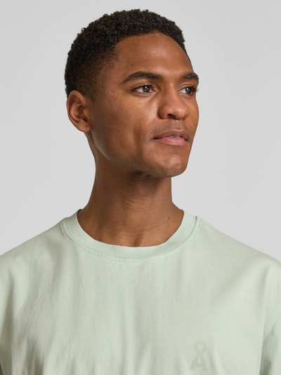 Männermodel trägt Relaxed Fit T-Shirt aus reiner Bio-Baumwolle Modell 'ICONIC MAARKOS GD' von Armedangels in Optik: Unifarben, Logo-Print, Rundhals, Kurzarm, Materialverarbeitung: Jersey, Nahaufnahme Oberkörper.