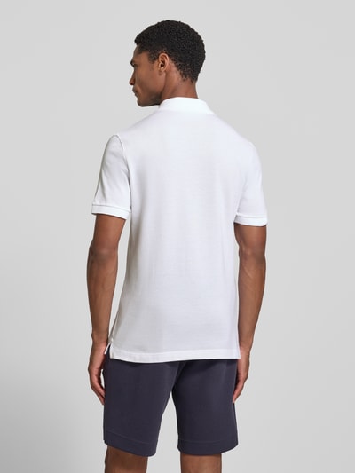 Männermodel trägt weißes Slim Fit Poloshirt aus reiner Baumwolle von Lacoste, glatte Textur, dunkelblaue Shorts, Ganzkörperansicht Rückansicht.