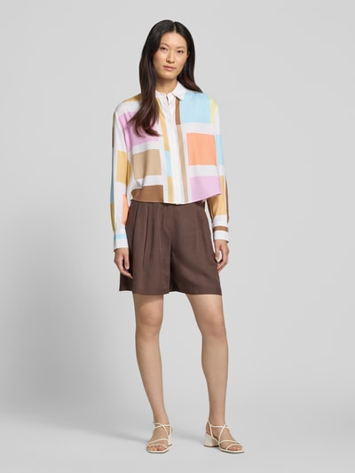 Modelka nosi Boxy Fit Bluse im Allover-Look od HERZENS, mieszanka materiałów z dodatkiem streczu, kołnierzyk koszulowy, listwa guzikowa, długość tyłu w rozmiarze 36: 59 cm, długość rękawów w rozmiarze 36: 61 cm, pastelowe kolory, geometryczne kształty, gładka faktura, widok całej sylwetki z przodu.