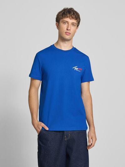 Männermodel trägt Slim Fit T-Shirt aus reiner Baumwolle von Tommy Jeans in kräftigem Blau, glatte Textur, Ganzkörperansicht von vorne. Herren T-Shirt von Tommy Jeans.