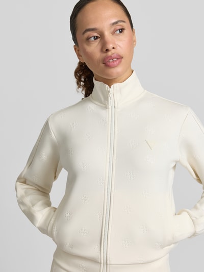 Frauenmodel trägt Sweatjacke mit Logo-Muster Modell 'CALISTA' von Guess Activewear in Beige, Material-Mix mit Stretch-Anteil, Regular-Fit, Stehkragen, Reißverschluss, Eingrifftaschen, Nahaufnahme Oberkörper.