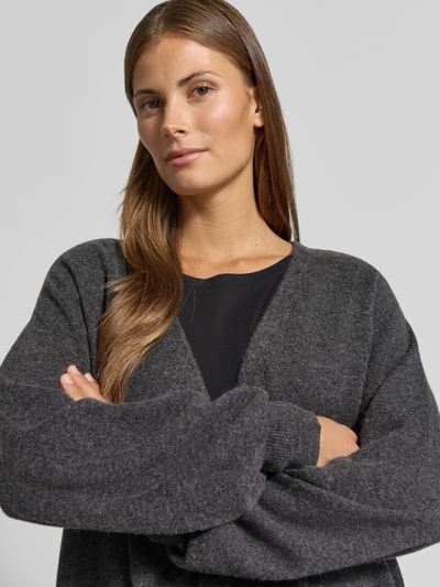 Vrouwenmodel draagt Strickjacke aus Lanawolle-Kaschmir-Mix Modell 'CESTINO' van Max Mara, donkere grijstinten, losse fit, diepe V-hals, geribde boorden, mix van zachte texturen, midde opbouw, Nahaufnahme Oberkörper.