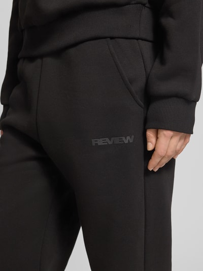Frauenmodel trägt Basic Sweatpant mit Bündchen am Saum und seitlichen Taschen von Review, schwarzer Baumwoll-Mix, Label-Print, Nahaufnahme Oberkörper.