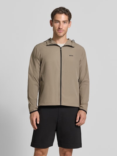 Männermodel trägt Regular Fit Trainingsjacke mit Label-Print Modell 'OW_Airynix JT HD 2' von BOSS Green in Beige und Schwarz, Ganzkörperansicht von vorne.