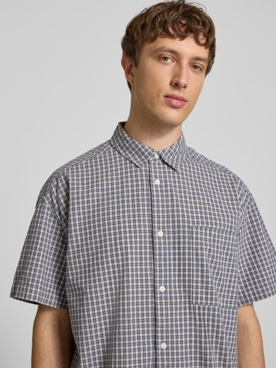 Männermodel trägt Loose Fit Freizeithemd aus reiner Baumwolle Modell 'DAVES' von Only & Sons im karierten Allover-Muster mit Kentkragen, einreihiger Knopfleiste, Kurzarm und Brusttasche, Material wirkt leicht strukturiert, Nahaufnahme Oberkörper.