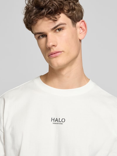Männermodel trägt Boxy Fit T-Shirt mit Label-Print von ELITE in Weiß aus Baumwolle, Rundhalsausschnitt, Nahaufnahme Oberkörper.