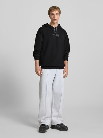 Männermodel trägt Hoodie mit Logo von PUMA PERFORMANCE, schwarz, Relaxed Fit, Kapuze, Material-Mix, Ganzkörperansicht von vorne.