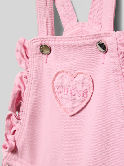 Mädchen trägt Regular Fit Latzhose in Denim-Optik von Guess, reine Baumwolle, 5-Pocket-Design, Logo-Stitching, Rüschenbesatz, Detailaufnahme