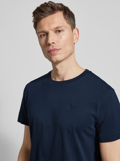 Männermodel trägt Regular Fit T-Shirt aus reiner Baumwolle von Tom Tailor in Dunkelblau, unifarben, mit Logo-Stitching, Nahaufnahme Oberkörper.