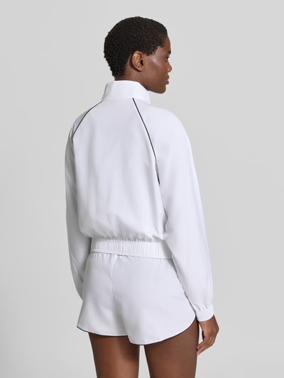 Frauenmodel trägt Relaxed Fit Trainingsjacke mit Logo-Patch von Lacoste in Weiß mit schwarzen Details, glatte Textur, Damen Trainingsjacke, Ganzkörperansicht Rückansicht.