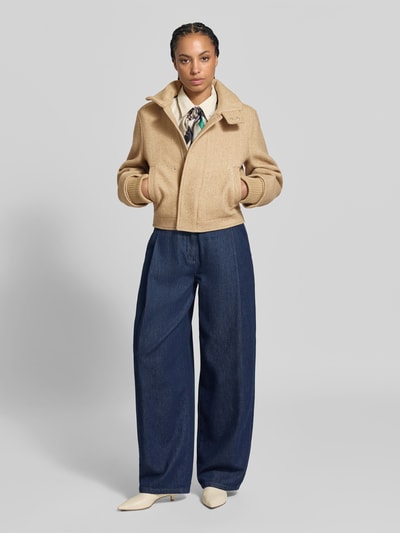 Frauenmodel trägt Bomberjacke aus Woll-Mix von Victoria Beckham in Beige, Regular Fit, Stehkragen, elastische Ärmelabschlüsse, Eingrifftaschen, kombiniert mit weiter dunkelblauer Hose und beigen Schuhen, Ganzkörperansicht von vorne. Rückenlänge bei Größe 36: 56 cm, Brustweite: 48 cm, Ärmellänge: 67 cm.