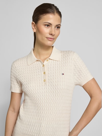 Vrouwenmodel draagt 'Slim Fit Poloshirt aus reiner Baumwolle' van Tommy Hilfiger, effen kleur, kabelpatroon, logodetail, korte mouw, polokraag, v-hals, knoopsluiting, knitwear van puur katoen, detailopname bovenlichaam.