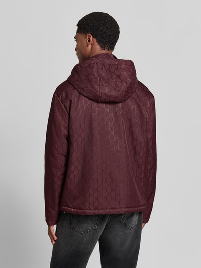 Männermodel trägt Regular Fit Jacke mit Allover-Logo-Print von Emporio Armani in Dunkelrot mit Kapuze, Rückenansicht, Ganzkörperansicht Rückansicht.