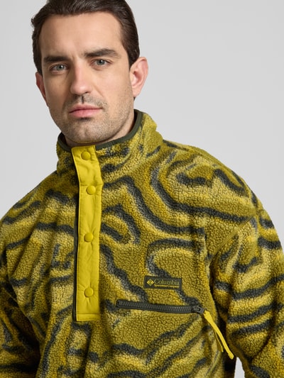 Männermodel trägt Regular Fit Pullover mit Logo-Patch von Columbia in grün-gelber Fließ-Optik, Reißverschluss-Brusttasche, Nahaufnahme Oberkörper. Rückenlänge 72 cm, Ärmellänge 49 cm, Stehkragen mit Druckknopfleiste, elastische Abschlüsse.