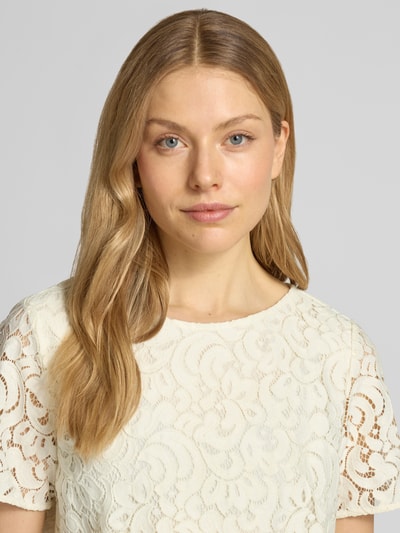 Kobiece modelka nosi Regular Fit Bluse mit Baumwoll-Anteil von s.Oliver BLACK LABEL, jednolity kolor, krój regular fit, wzór: detale z koronki z kwiatowym wzorem, długość: krótki krój, detale: półprzezroczyste detale z koronki, dekolt w łódkę, zapięcie na 1 guzik, rękaw: krótki rękaw, jasny kremowy kolor, wyrazista tekstura koronki, półmatowa powierzchnia, detaliczne zdobienia, nahaufnahme górnej części ciała.