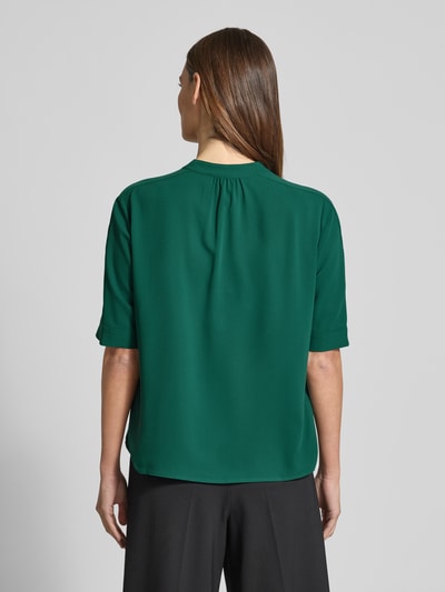 Modelka kobieca ma na sobie Regular Fit Bluse mit V-Ausschnitt od Marc Cain, zielona z krótkim rękawem, krój regular fit, długość tyłu 59 cm, długość rękawa 29 cm, widok całej sylwetki z tyłu.
