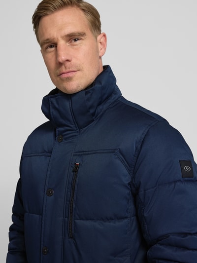 Męski model nosi Regular Fit Steppjacke mit Kapuze od Tom Tailor, granatowa, gładka, stójka z kapturem, zamek kryty, długie rękawy, naszywka, kieszenie, zbliżenie na górną część ciała