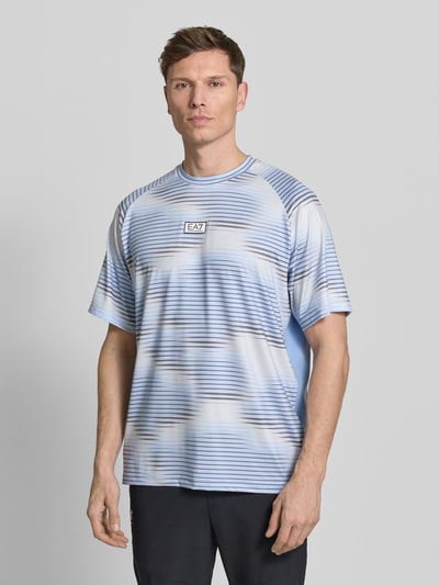Männermodel trägt Regular Fit T-Shirt mit Logo-Applikation von EA7 Emporio Armani, blau gemustert, elastischer Mix, Nahaufnahme Oberkörper.