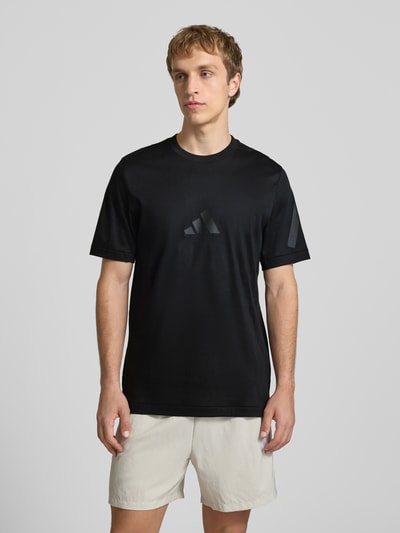 Męskimodel nosi Regular Fit T-Shirt aus reiner Baumwolle od adidas Sportswear, jednokolorowy czarny, nadruk z logo, okrągły dekolt, krótki rękaw, bawełna, Ganzkörperansicht von vorne.