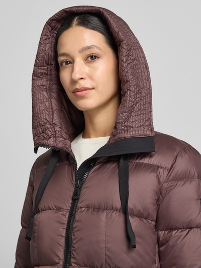 Frauenmodel trägt Daunenmantel mit Kapuze Modell 'NUNKI' von Peuterey in Braun mit Steppnähten und Zweiwege-Reißverschluss, Nahaufnahme Oberkörper.