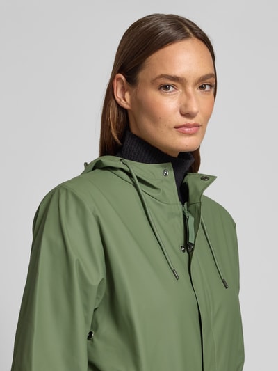 Kobiece modelka nosi Regular Fit Parker z kapturem model 'Fishtail' od Rains, zielony, gładka faktura, detal kaptura, zbliżenie na górę. Damski płaszcz z kapturem, tunel, krój regular fit, model 'Fishtail', kieszenie z patką, elastyczne zakończenia rękawów, długość tyłu w rozmiarze S: 104 cm, szerokość ramion w rozmiarze S: 45 cm, szerokość klatki piersiowej w rozmiarze S: 55 cm, długość rękawów w rozmiarze S: 65 cm