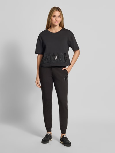 Vrouwenmodel draagt t-shirt met paillettenbesatz van Armani Exchange, puur katoen, los model, ronde hals, labelprint, ruglengte maat S 45 cm, geheel van voren te zien.
