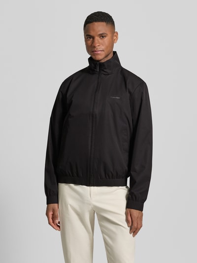 Männermodel trägt Jacke mit Stehkragen und Logo von CK Calvin Klein in Schwarz, Regular Fit, Reißverschluss, Eingrifftaschen, Nahaufnahme Oberkörper