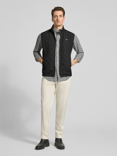 Männermodel trägt Regular Fit Weste mit Stehkragen in Stepp-Optik von Gant, schwarz, Logo-Stitching, Reißverschluss, Ganzkörperansicht von vorne.