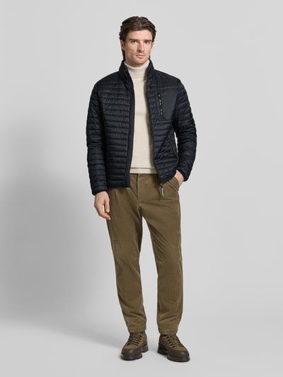 Männermodel trägt Steppjacke mit Stehkragen von camel active in Schwarz, schlichte Struktur, kombiniert mit heller Hose, Ganzkörperansicht von vorne, Regular Fit, Reißverschluss und Reißverschlusstaschen, Maße Größe M: Rückenlänge 27 cm, Schulterbreite 19 cm, Brustweite 22 cm, Ärmellänge 27 cm.
