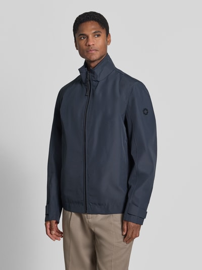 Männermodel trägt kurtka funkcyjna Regular Fit Funktionsjacke aus wasserdichtem Material Model 'LUCCA' von Strellson, jednokolorowy granatowy, długi rękaw z patkami, stójka, zamek błyskawiczny, metalowa aplikacja z logo, boczne kieszenie zapinane na zamek, krój regular fit, materiał wodoodporny i wiatroszczelny, Ganzkörperansicht von vorne.