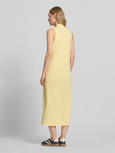 Modelka nosi Figurumschmeichelndes Polokleid aus Baumwoll-Mix von Polo Ralph Lauren w jednolitym jasnożółtym kolorze, bez rękawów, długość midi, materiał piké z bocznym rozcięciem, widoczne logo, całkowity widok z tyłu.