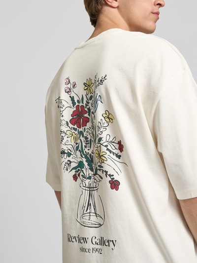 Männermodel trägt T-Shirt mit Stitching und Rundhalsausschnitt von REVIEW in Oversized-Passform, cremefarben, floraler Print hinten, Ganzkörperansicht Rückansicht.