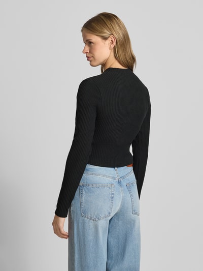 Frauenmodel trägt Cardigan in Ripp-Optik Modell 'CHILL' von Nike in Schwarz mit Skinny-Fit, Stehkragen, Label-Stitching, langärmelig, durchgehende Knopfleiste, Ganzkörperansicht Rückansicht.