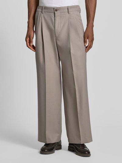 Männermodel trägt Wide Fit Hose mit Bügelfalten von Drykorn aus Baumwoll-Mix mit Stretch-Anteil in Beige, Nahaufnahme Vorderansicht.