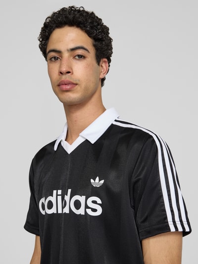 Männermodel trägt Regular Fit Trikot-Shirt mit Polokragen von adidas Originals, Optik: Unifarben, Label-Schriftzug, Kontraststreifen, V-Ausschnitt, Kurzarm; Nahaufnahme Oberkörper.