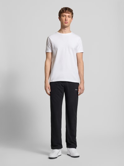 Männermodel trägt Sweatpants mit elastischem Bund von CHAMPION, lockerer Schnitt, Label-Stitching, schwarze Farbe, Ganzkörperansicht von vorne.