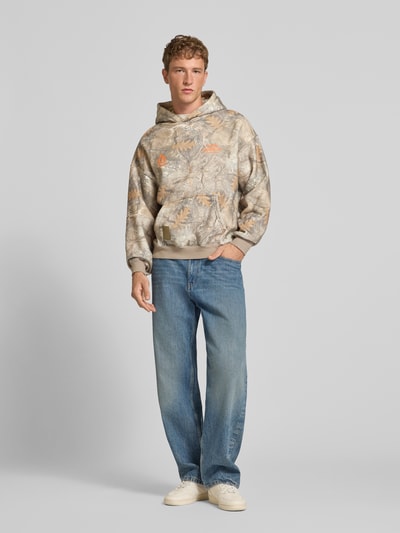 Männermodel trägt Hoodie mit Logo- und Motiv-Print von ANOTHER COTTON LAB, lockere Passform, Baumwoll-Mix, Naturtöne, Ganzkörperansicht von vorne.