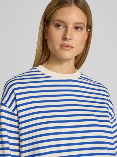 Modelka prezentuje bluzę Oversized Sweatshirt aus reiner Baumwolle Modell 'FRANKA MAARLEN' od Armedangels, dwukolorowy wzór w paski, wyhaftowane logo, okrągły dekolt, długi rękaw, wykończenie: dzianina dresowa, materiał: czysta bawełna. Zbliżenie na górną część ciała.