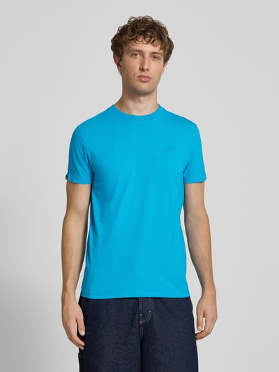 Männermodel trägt T-Shirt mit Rundhalsausschnitt und Label-Stitching von Superdry, reine Baumwolle, Slim Fit, Ganzkörperansicht von vorne.